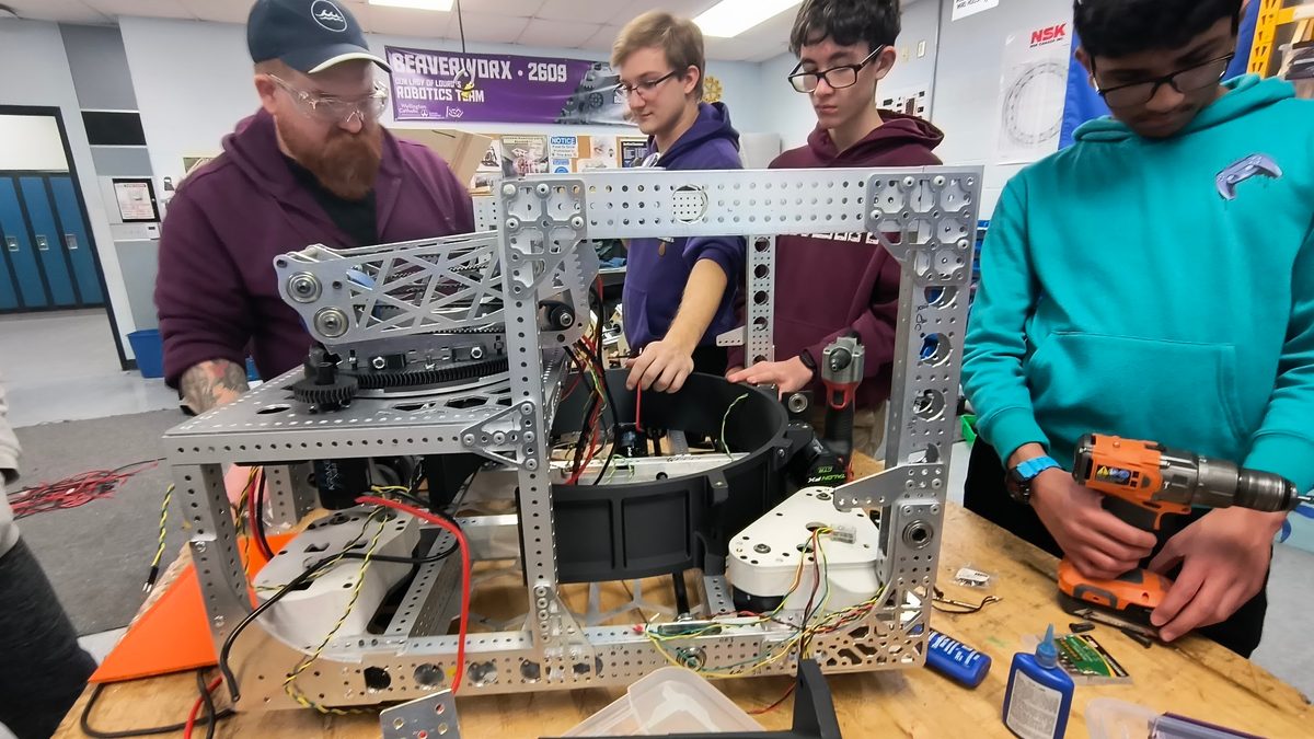 A mentor and a group of students working together on a larger FRC competition robot