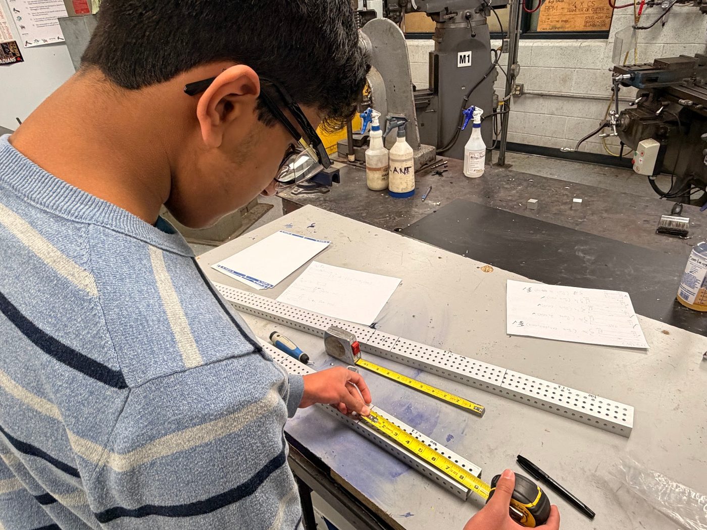 A student measuring and marking a piece of aluminum extrusion for a robot build