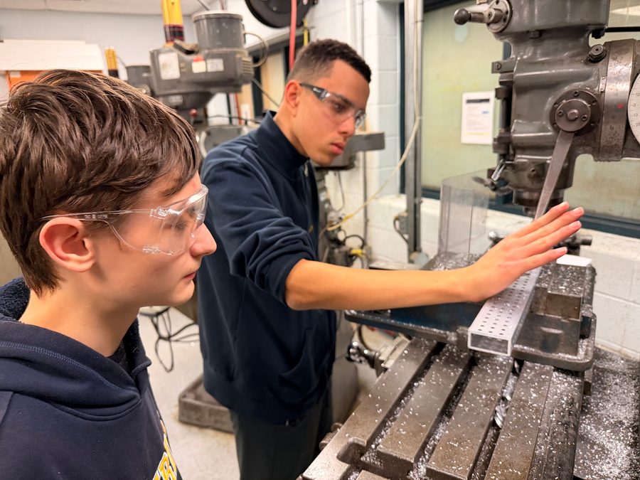 An older student showing a newer student how to use a milling machine